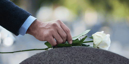 SURNE-fallecimiento-de-autonomo Mano de hombre depositando una rosa sobre una tumba