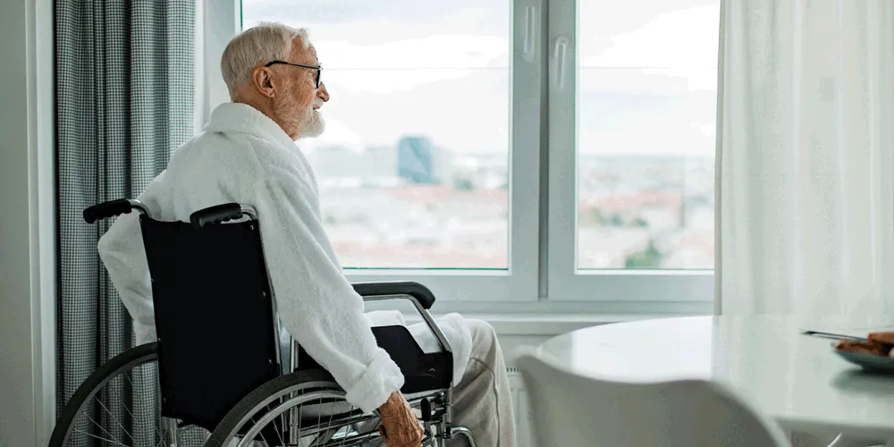 Hombre en silla de ruedas mirando por la ventana