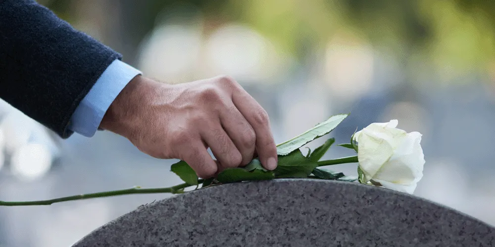 SURNE-fallecimiento-de-autonomo Mano de hombre depositando una rosa sobre una tumba
